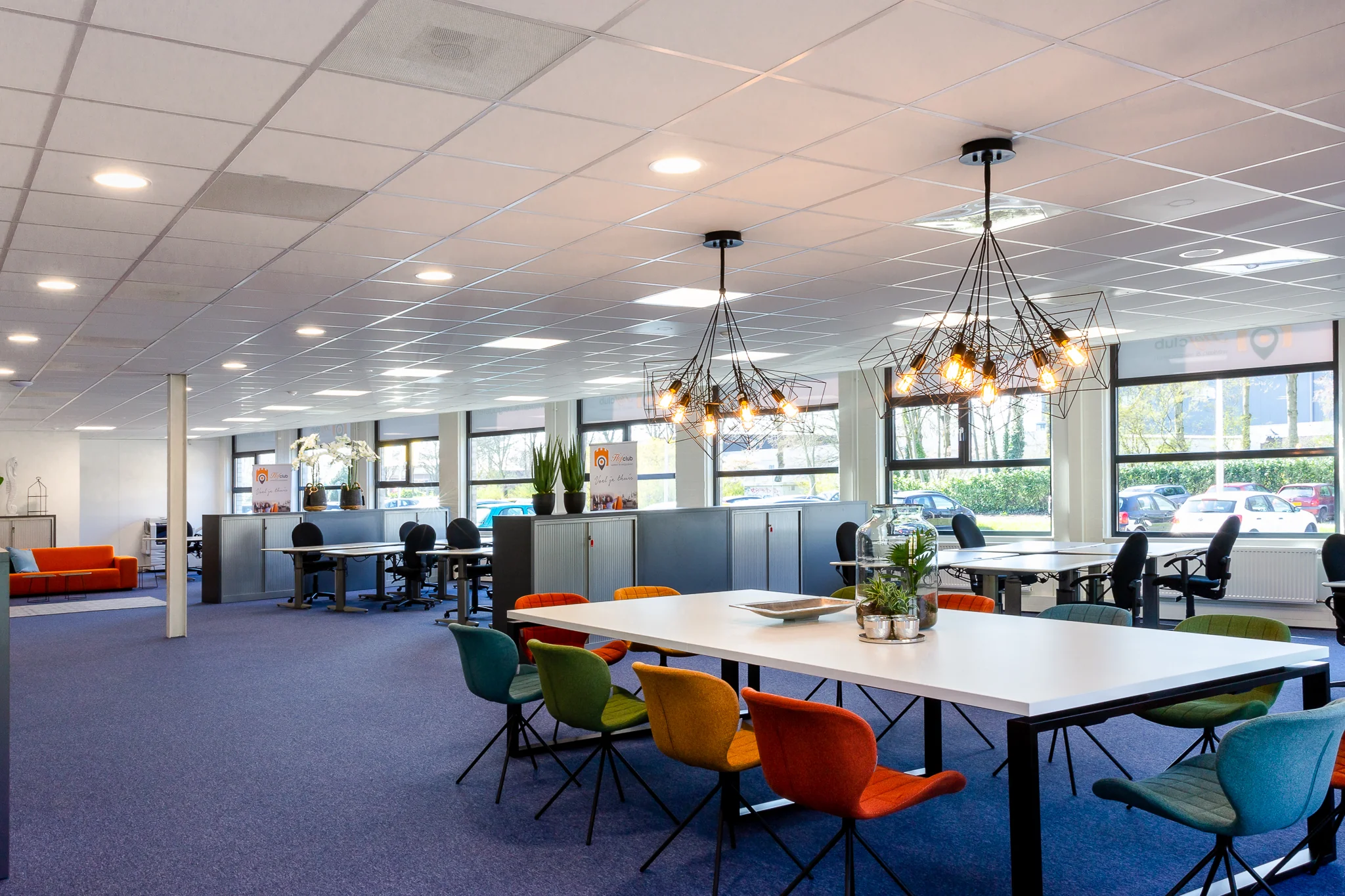 Moderne kantoortuin aan de Niels Bohrweg met kleurrijke stoelen, open werkplekken en industriële hanglampen.